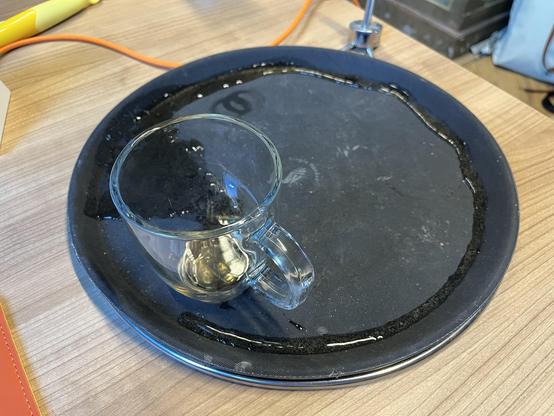 An empty glass tea cup on a black serving platter. Contrary to the intended use of tea cups, the beverage in question is scattered over the surface of the platter, rather than inside the cup.