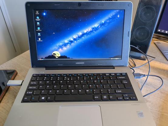 A photo of a netbook with the desktop screen of Lubuntu. It shows some icons and a photo of the Milky Way and the Moon as a background.