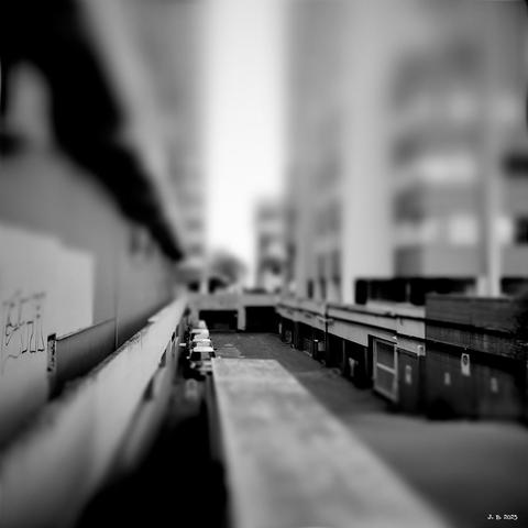 Black and white photograph of a back alley with garages below and tall buildings on the left and right.