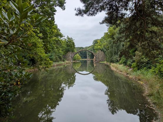 Rakotzbrücke mit Halbbogen über dem Wasser und symmetrische Spiegelung im See
