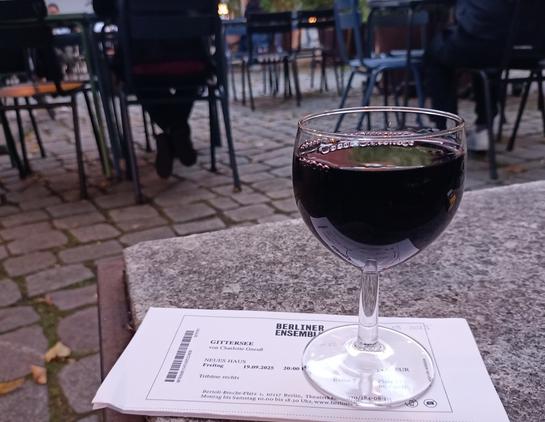 Das Ticket und ein Glas Rotwein auf einem Steintisch im Hof des Berliner Ensemble.