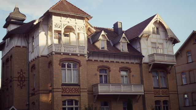 large yellow brick house with red brick patterns and white timber frame construction with wooden ornaments on the top floor