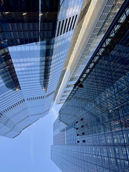 Upward view of modern glass skyscrapers in London with reflective surfaces against a clear blue sky, creating geometric patterns and reflections.