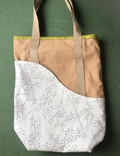 Einkaufstasche aus braunem und beigem Stoff auf einem grünen Tisch. Die Henkel sind auch geige. Eine Wellenlinie teilt die Tasche in zwei Segmente