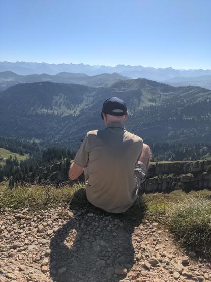 Mann mit Rücken zu Kamera sitzt vor Bergpanorama der Allgäuer Alpen