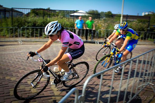 Photograph of three cyclists in a race. Marianne Vos is ahead at Draai van de Kaai 2011. Wielerpro.nl, CC BY 2.0 <https://creativecommons.org/licenses/by/2.0>, via Wikimedia Commons