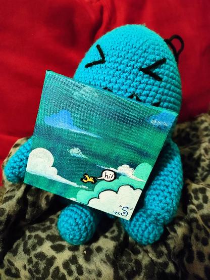 Svnnyne's signed 4"x4" painting of a small yellow bird flying "hi!" in an iridescent blue/teal/turquoise sky with blue and white clouds, being held by a crochet Wobbuffet grinning with glee on a blue leopard comforter against a red background.