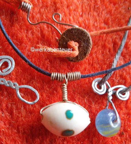 Auf rotem Teppich liegen einige Beispiele für Drahtbiegearbeiten, um Perlen an einer Kordel zu befestigen. Auch eine Schließe ist zu sehen.