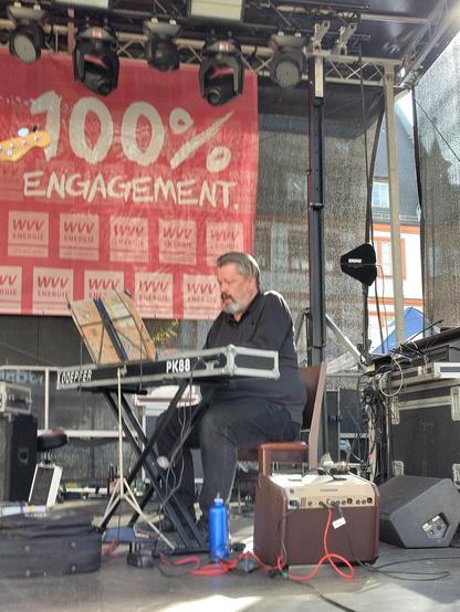 Ein Mann in schwarzer Kleidung und grau meliertem Haar sitzt auf einer Bühne an einem E-Piano und spielt konzentrierten Jazz.