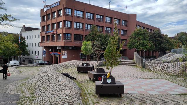 Drei Wanderbäume in ihren fahrbaren Kübeln mit Bank. Auf dem Europaplatz auf dem Ebenen Teil oben neben dem Nachhaltigkeitsberichtszentrum und gegenüber der Volksbank.