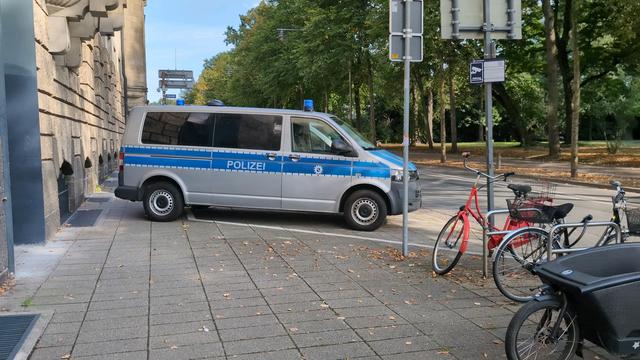 Ein Polizeibulli steht vor der Wache auf einem Parkplatz und lässt hinten nur wenig Gehwegbreite frei. Vorne ist noch viel Platz bis zur Straße.