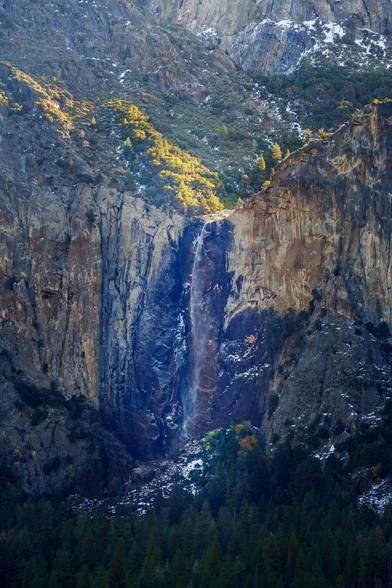 A waterfall cascading down a rocky cliff, surrounded by greenery and hints of autumn colors in the landscape.