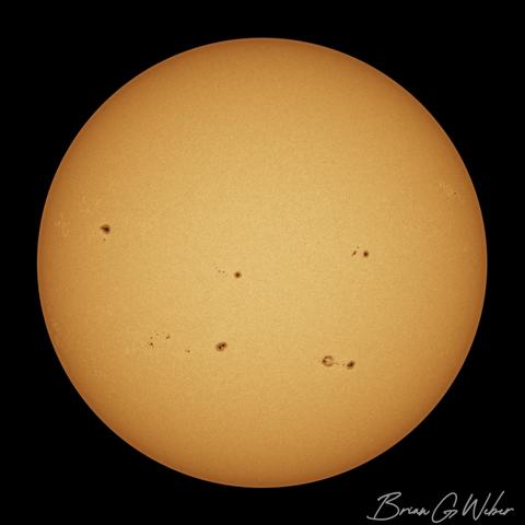 A full disk monochrome solar image colorized orange with a surface covered in sunspot clusters