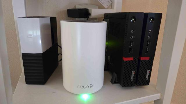 A photo of a shelf with two micro PCs standing vertical, a WD external drive, and a TPLink Deco WiFi AP.