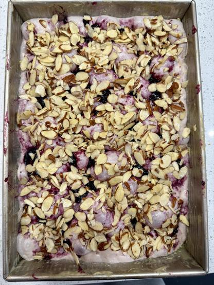 Uncooked focaccia with jam pressed into the dough and topped with slices of almond