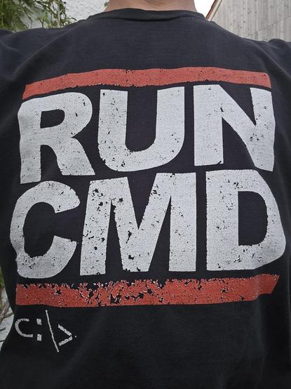 T-Shirt mit dem Logo von Run-DMC, aber mit vertauschten Buchstaben zu -CMD und unter dem Logo der Prompt C:\>