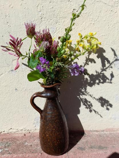 Mixed flowers from a meadow and my garden in purple, rose. And yellow. In a long dark brown pottery vase.