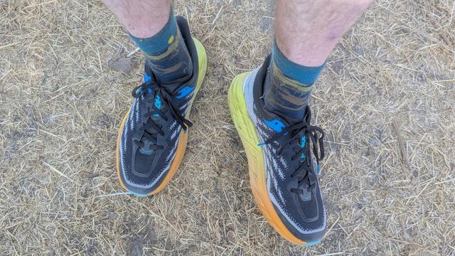 My feet in new shoes. The shoes have dark uppers with light gray highlights, with yellow and orange around the base. I am wearing crew length socks.