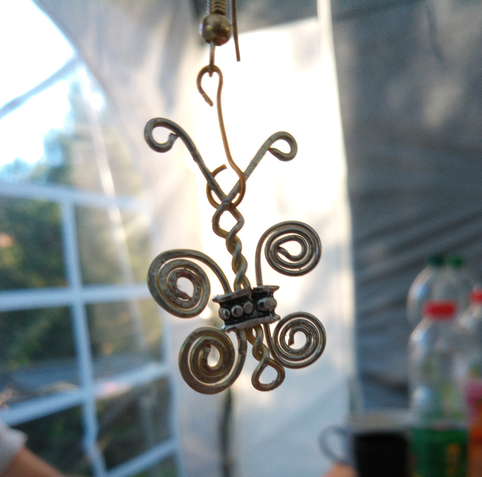 Ein aus Draht gebogener Schmetterling vor dem Weiß einer Zeltwand.