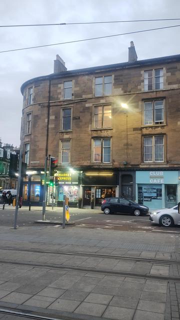 Looking across the road & tram tracks to a Victorian stone tenement opposite, street lights just coming on as dusk falls