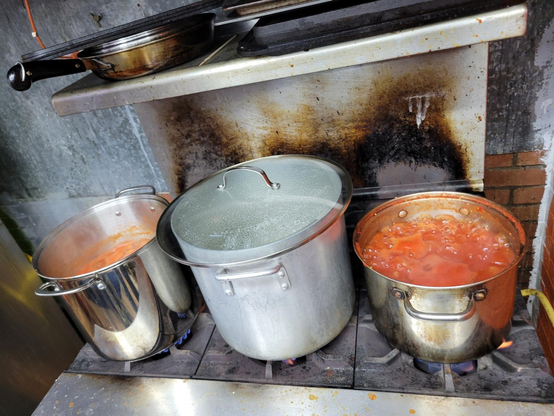 2 pots of pasta sauce and a pot of pasta on the stove