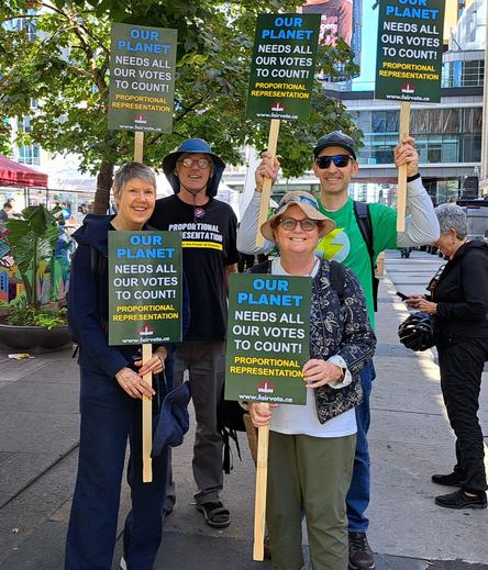 Four volunteers stand holding signs. The signs say "Our planet needs all our votes to count! Proportional Representation. fairvote.ca"