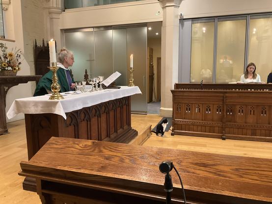 Black and white cat sitting upright near the altar during a communion service