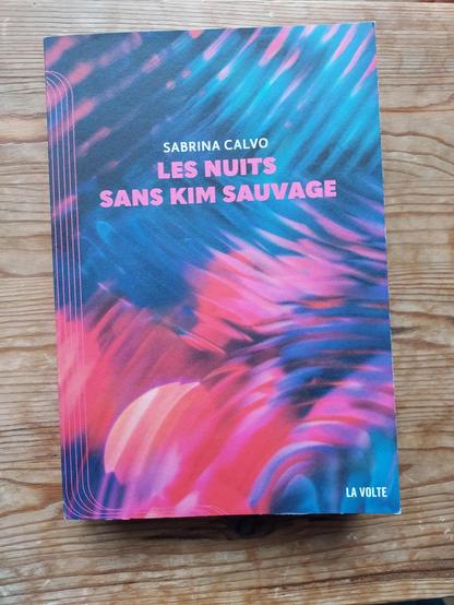 couverture de "Les nuit sans Kim Sauvage" de Sabrina Calvo.
Tout en majuscule
Titre sur deux lignes en rose surmonté du nom de l'autrice su une ligne.

l'image du fond en rose-orange et bleu sombre évoque une photo floue d'onde dans l'eau. (sans être vraiment représentatif.)