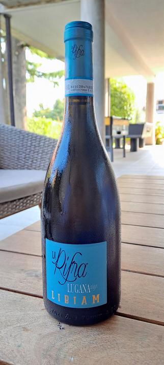 Bottiglia di vino Lugana poggiata su un tavolino di legno, all'interno di un patio con divanetti.