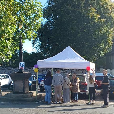 People standing around a table in a car park under a gazebo - the sun shining!