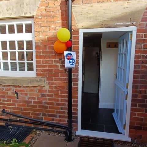 The door of a house one the right with a multi paned window to left. More balloons and another 35 sign on the drainpipe