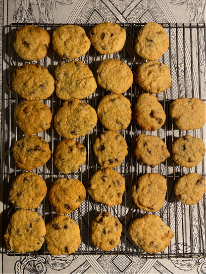 Color image of 27 freshly baked chocolate chip cookies cooling on a rack on an enamel kitchen table.