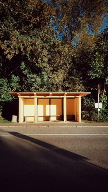An empty concrete bus stop in late summer light.