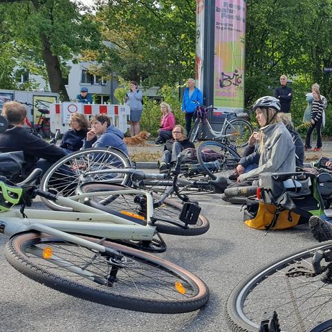Teilnehmende bei der Mahnwache knien und sitzen mit ihre  Fahrrädern an der Unfallstelle Berner Heerweg/Berner Allee