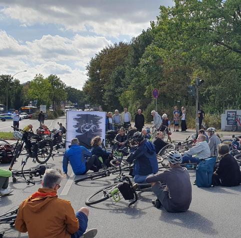 Teilnehmende bei der Mahnwache knien und sitzen mit ihre  Fahrrädern an der Unfallstelle Berner Heerweg/Berner Allee