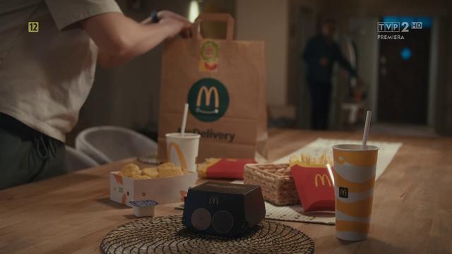 Paczka frytek, boxów i napojów z McDonald's, z torbą McDelivery w tle, na stole. Kacper zamówił dostawę z Maca na pojednawczą kolację z ojcem Ludwikiem.