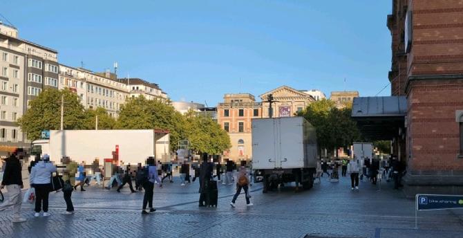 Mehrere LKW und ein Angestellter LKW-Anhänger auf dem Bahnhofsvorplatz. Dazwischen laufen viele Menschen.