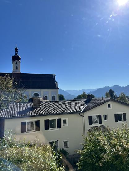 Die Sicht aus dem Damenklo des Schloss Museums Murnau, mit Kirchturm, links, den Bergen im Hintergrund und strahlend blauen Himmel