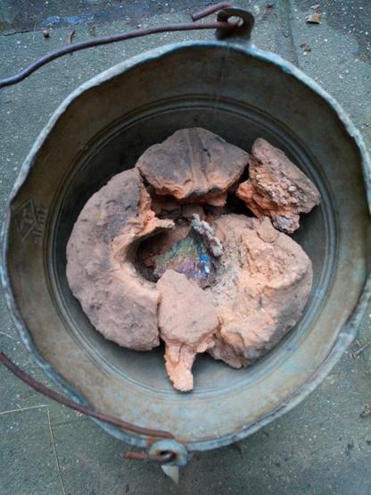 Blick von oben in einen Blecheimer, in dem ziegelrote Bruchstücke eines Ofens liegen. In der Mitte liegt ein verglastes, farbiges Bruchstück des Schlotes.