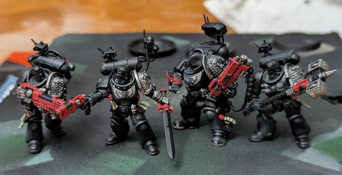 Four Primaris Deathwatch Space Marines. Painted black with some silver and red popping details.