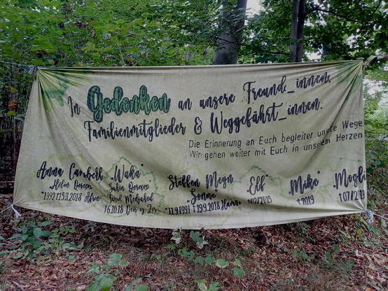 zwischen Bäumen im Hambacher Wald hängt ein Banner in Gedenken an  verstorbene Mitstreiter*innen