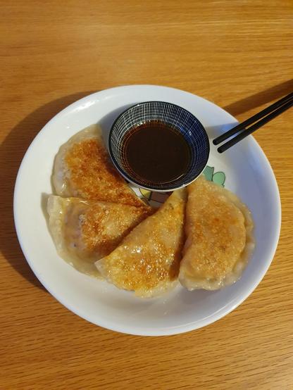 Vier stücken Mandu mit Sojasoße +Sesamöl im kleinen weißen Schüsselchen und schwarzes Stäbchen auf dem Holztisch