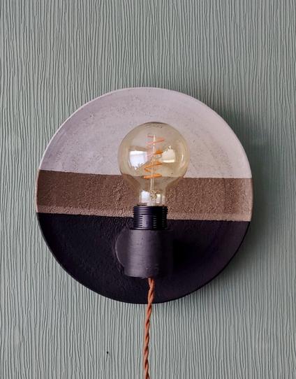 a plate shaped ceramic wall sconce with an edison bulb. The top is glazed shiny white, the bottom with a matte black
