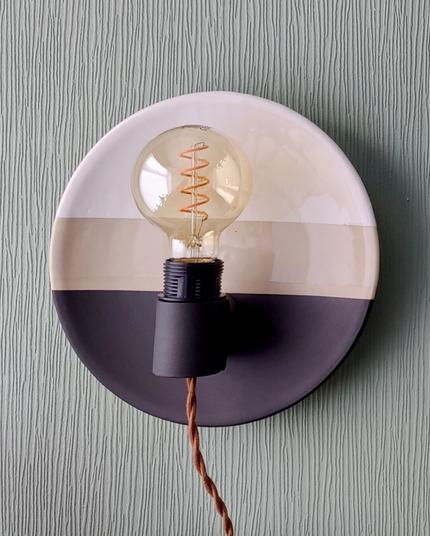 a plate shaped ceramic wall sconce with an edison bulb. The top is glazed shiny white, the bottom with a matte black