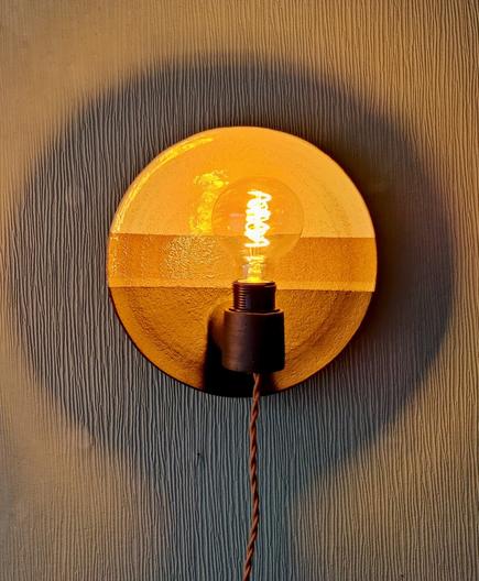 a plate shaped ceramic wall sconce with an edison bulb showing how it looks when lit. The top is glazed shiny white, the bottom with a matte black