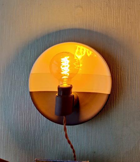 a plate shaped ceramic wall sconce with an edison bulb showing how it looks when lit. The top is glazed shiny white, the bottom with a matte black