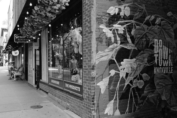 Black and white photo of a brick building currently housing a dispensary and the Coffee & Chocolate shop next door. Some graffiti on the corner of the building is dedicated to Downtown Knoxville.
