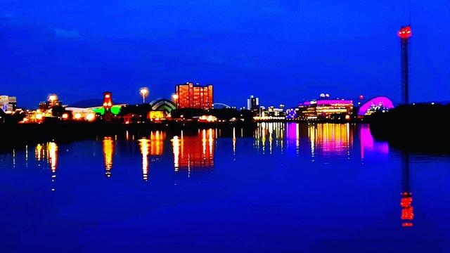 Modern buildings lit up at bight and reflected in the still waters of the Clyde.