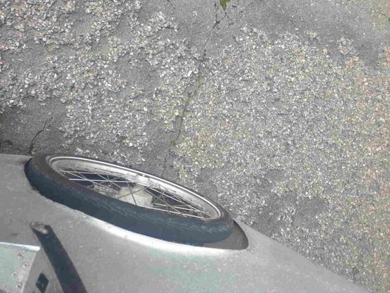 Détail près de la roue avant de vélomobile, et vue sur un revêtement routier belge fait d'une sorte de gravier glissant irrégulier collé à du bitume.