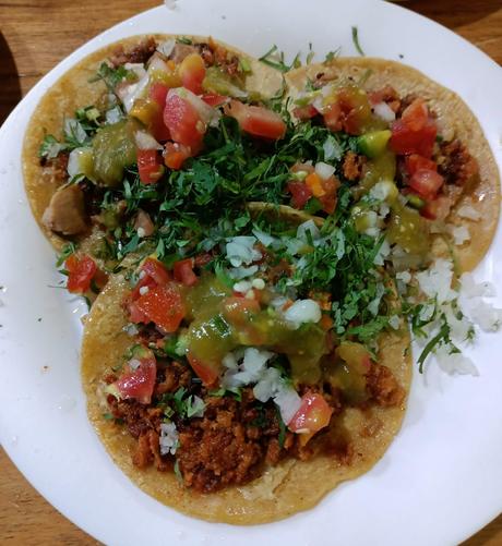 a photo of three mexican tacos served with onion, tomate, coriander and green sauce.